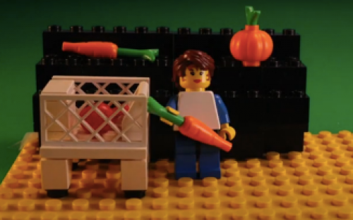 Lego person standing with carrots and a crate of food