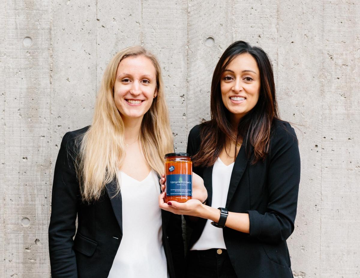 Photo of Laura Frielingsdorf and Kiran Bains holding a jar of Upcycle Kitchen tomato sauce.