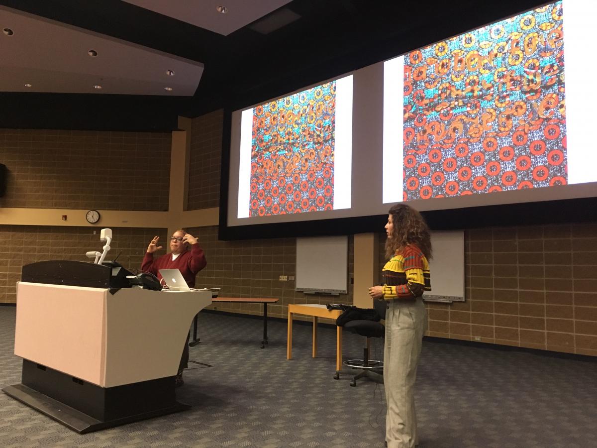 Photo showing Syrus Ware, artist and activist, presenting in Saba Safdar's Social Psychology class. The picture shows Syrus, Saba, and a large screen with a picture of colourful art. Students are not visible on the image.