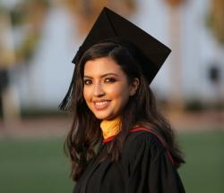Woman with long dark hair wearing graduation gown and cap, smiling
