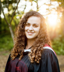 Woman with curly brown hair wearing graduation gown, smiling