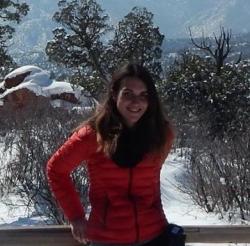 Individual with long dark hair wearing a red puffy jacket standing outside in winter, smiling