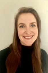 Woman with long brown hair wearing a black turtleneck sweater smiles at the camera.