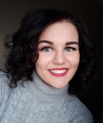 Woman with dark hair wearing a grey turtleneck and pink lipstick, smiling