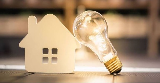 A house-shaped model beside a glowing light bulb, representing residential energy use and energy efficiency.