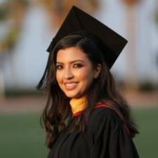 Woman with long dark hair wearing graduation gown and cap, smiling