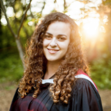 Woman with curly brown hair wearing graduation gown, smiling