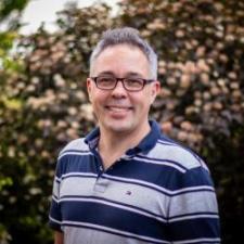 Headshot of Craig Johnson; man wearing glasses and a striped polo shirt.