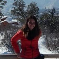 Individual with long dark hair wearing a red puffy jacket standing outside in winter, smiling