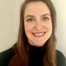 Woman with long brown hair wearing a black turtleneck sweater smiles at the camera.