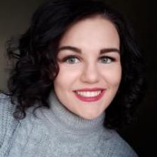 Woman with dark hair wearing a grey turtleneck and pink lipstick, smiling