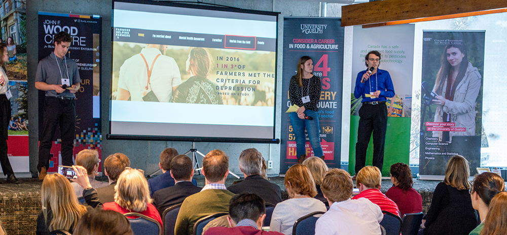 Three students standing beside a PowerPoint presentation, pitching their solution at the Improve Life Challenge.