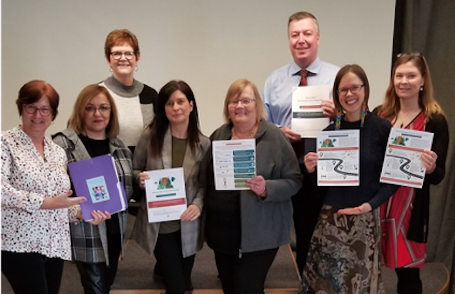 Photo shows a group of 8 people smiling and holding paper reports.