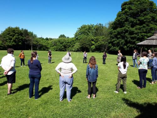 Approximately 20 people stand in a circle in a field; it is summer.